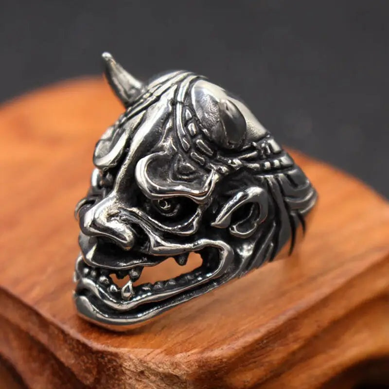 Zilverkleurige ring met Oni-demonenmasker en hoorns, liggend op houten standaard | Boutique Moda