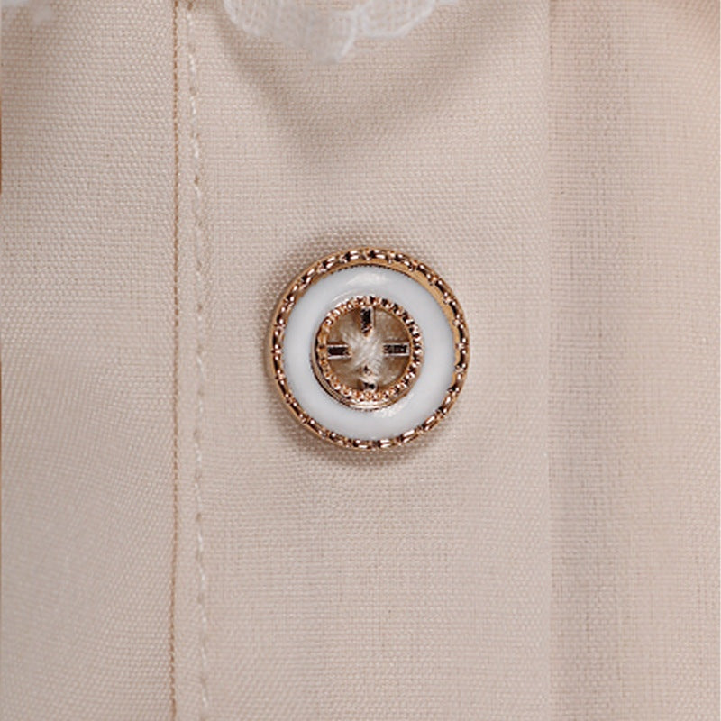 Close-up van gouden knoop met wit emaille op beige overhemdstof | Boutique Moda