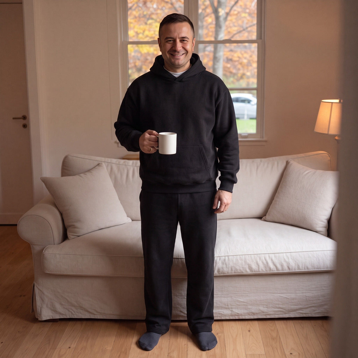 Man draagt zwart joggingpak met hoodie en mok koffie thuis | Boutique Moda