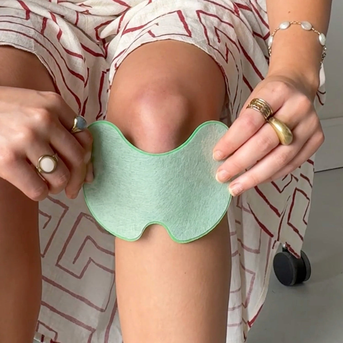 Groene zelfklevende kniepleister aangebracht op knie van zittend persoon | Boutique Moda