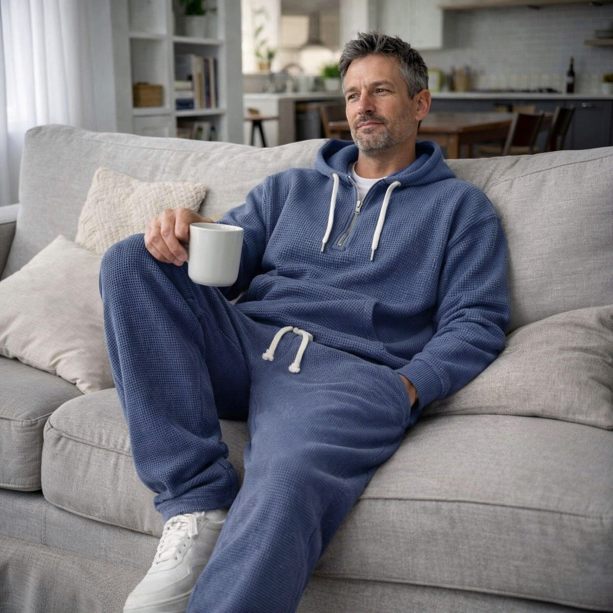 Man draagt blauw trainingspak met hoodie, zittend op bank met koffie | Boutique Moda