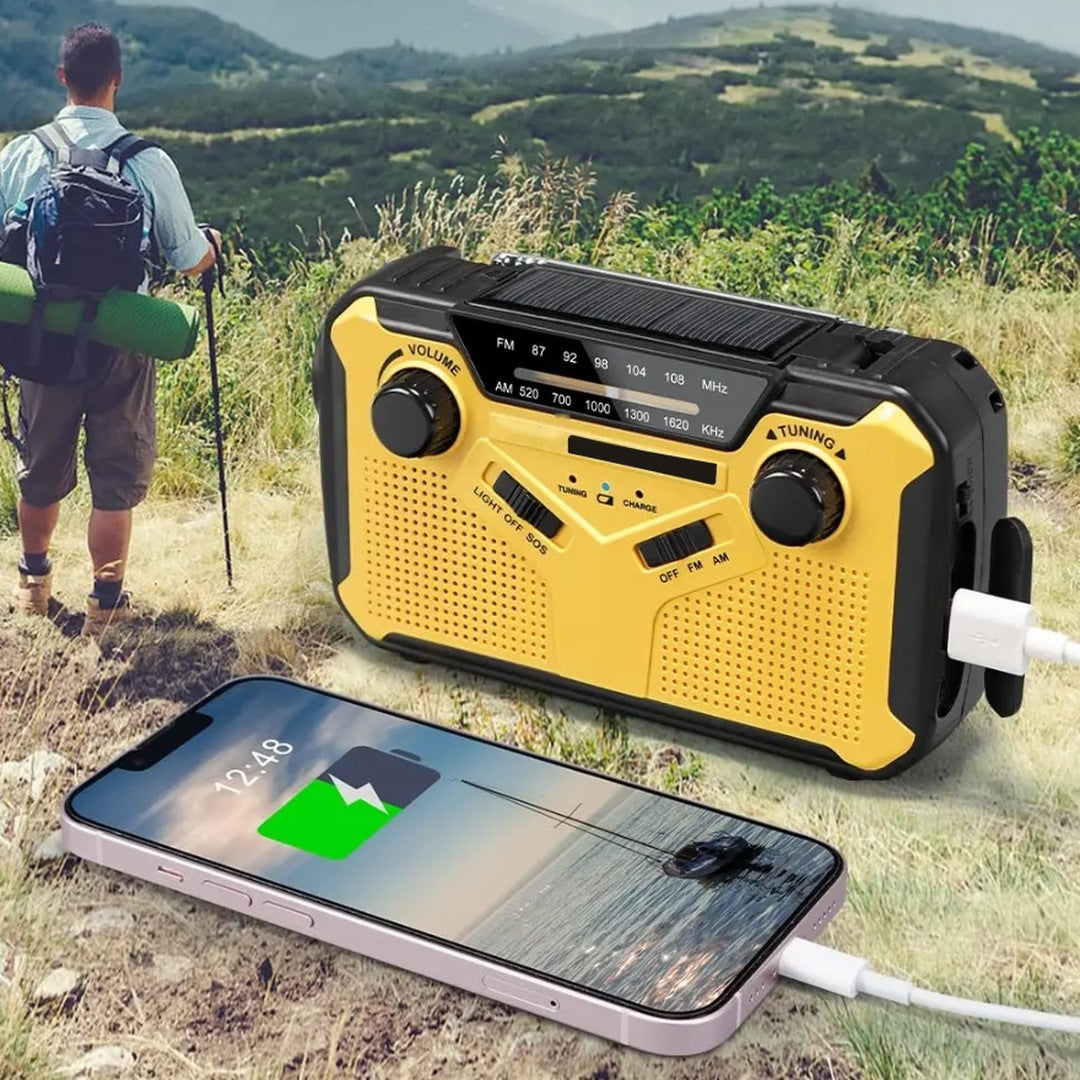 Gele noodradio met zonnepaneel laadt smartphone op buiten in natuur | Boutique Moda
