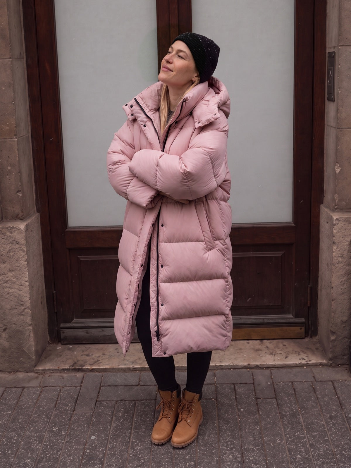 Vrouw in een roze lange pufferjas met capuchon voor een houten deur