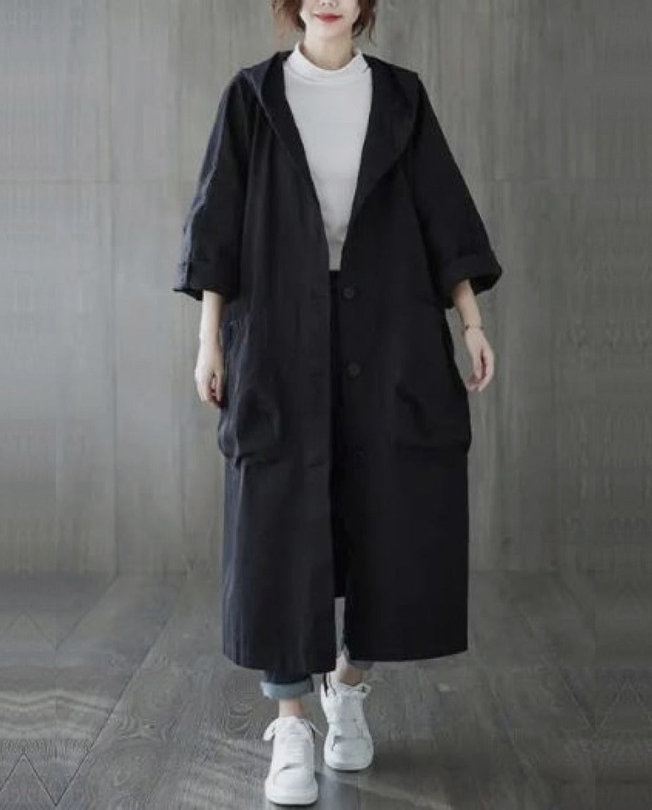 Zwarte lange oversized regenjas met capuchon, gedragen door vrouw met sneakers | Boutique Moda