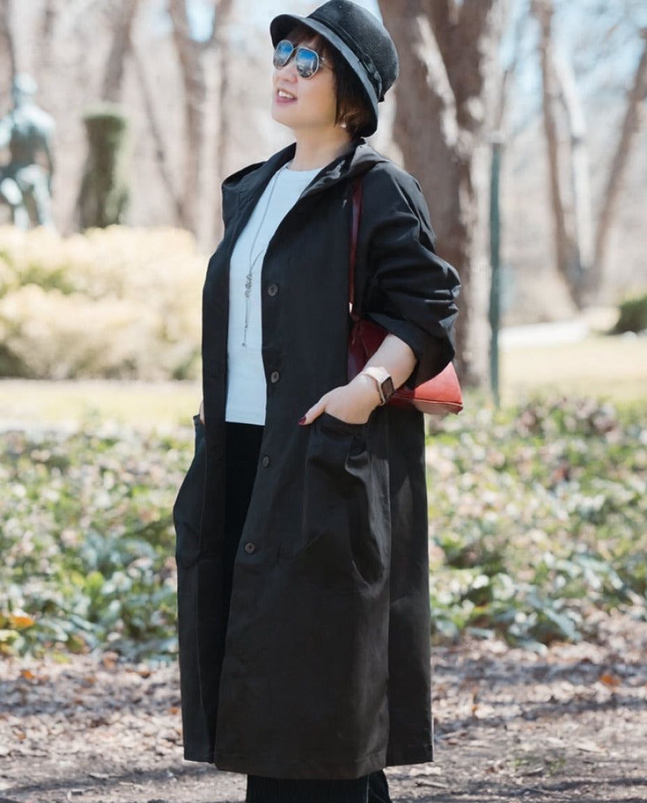 Zwarte oversized regenjas gedragen door vrouw met hoed in park | Boutique Moda