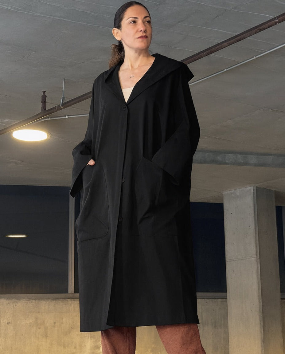 Zwarte oversized regenjas met capuchon, gedragen door vrouw in parkeergarage | Boutique Moda