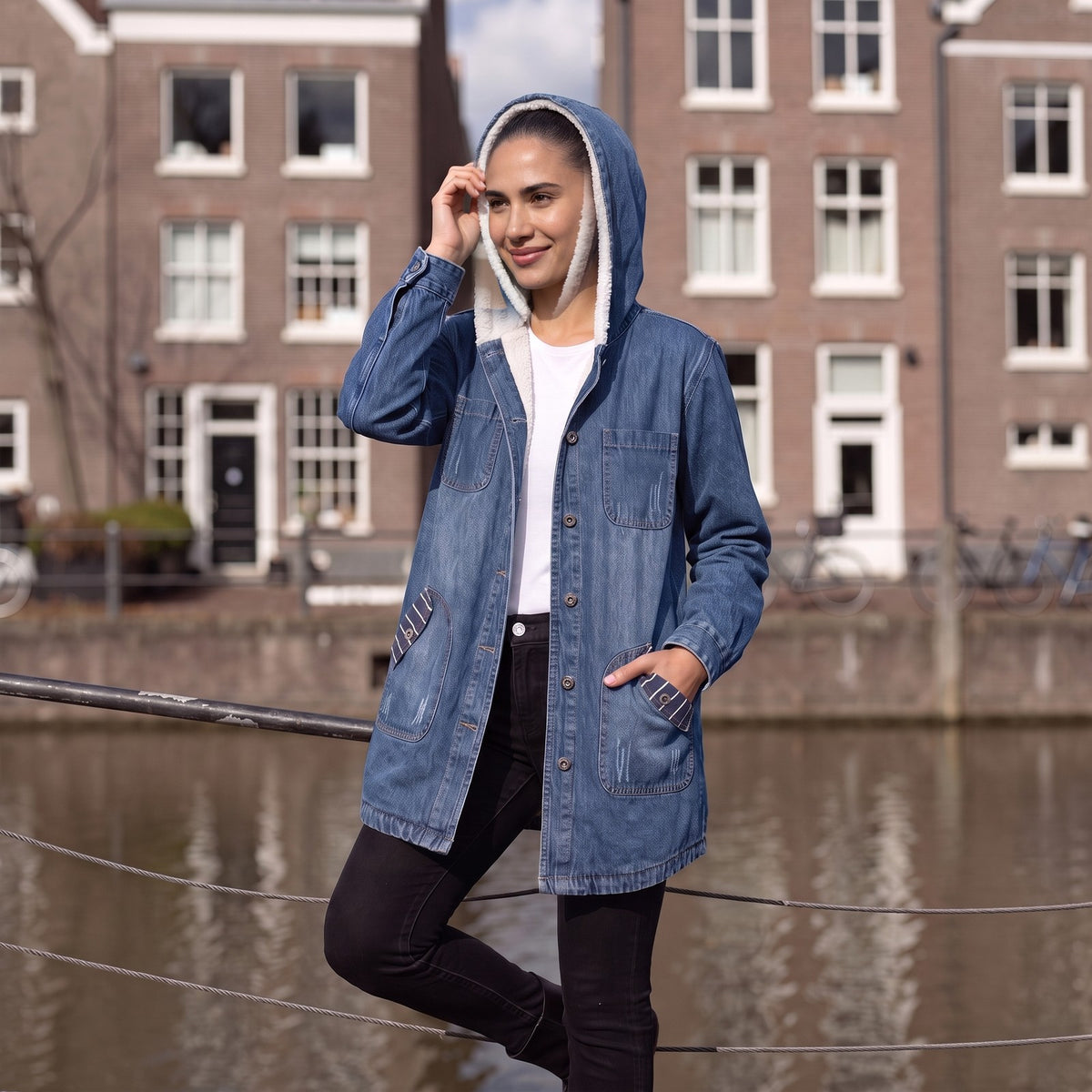 Vrouw in een lange spijkerjas met teddyvoering en capuchon langs een gracht in Den Haag