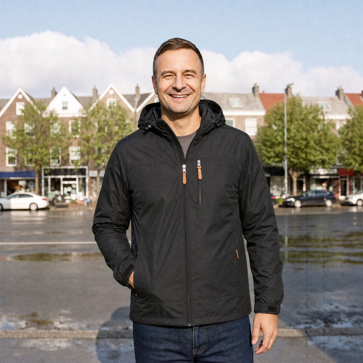 Zwarte winddichte outdoorjas met capuchon, gedragen door glimlachende man buiten | Boutique Moda