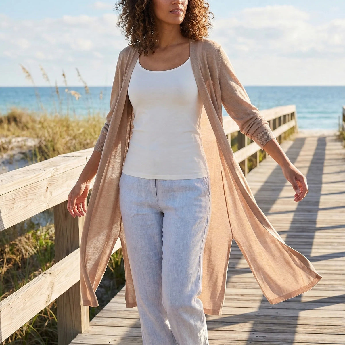 Vrouw op een strandvlonder in een lang open vest in camel | Boutique Moda