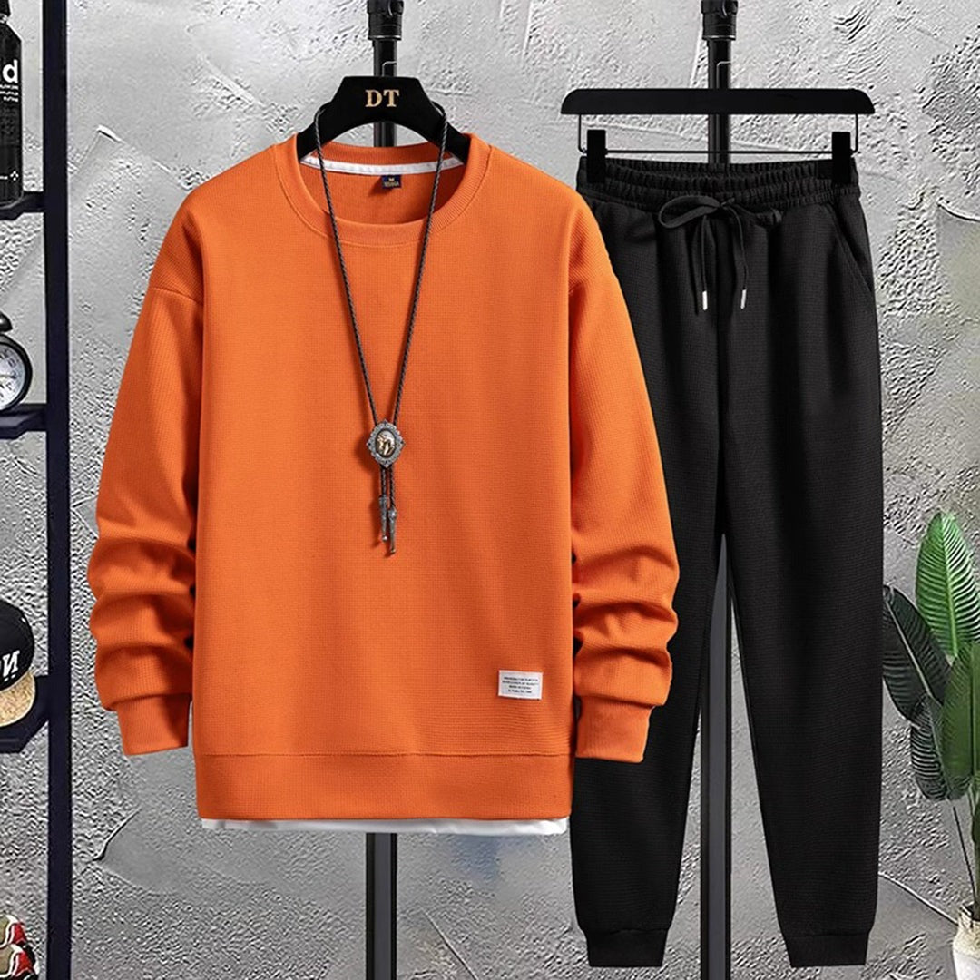 Oranje sweater met wafelstructuur en zwarte joggingbroek aan hangers | Boutique Moda