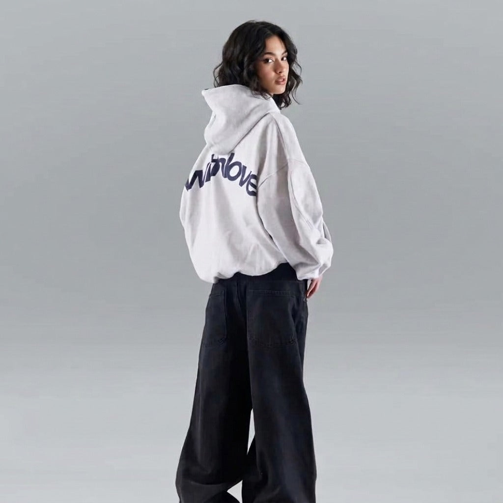 Vrouw in een grijze oversized hoodie met een grote rugprint en een wijde zwarte broek | Boutique Moda