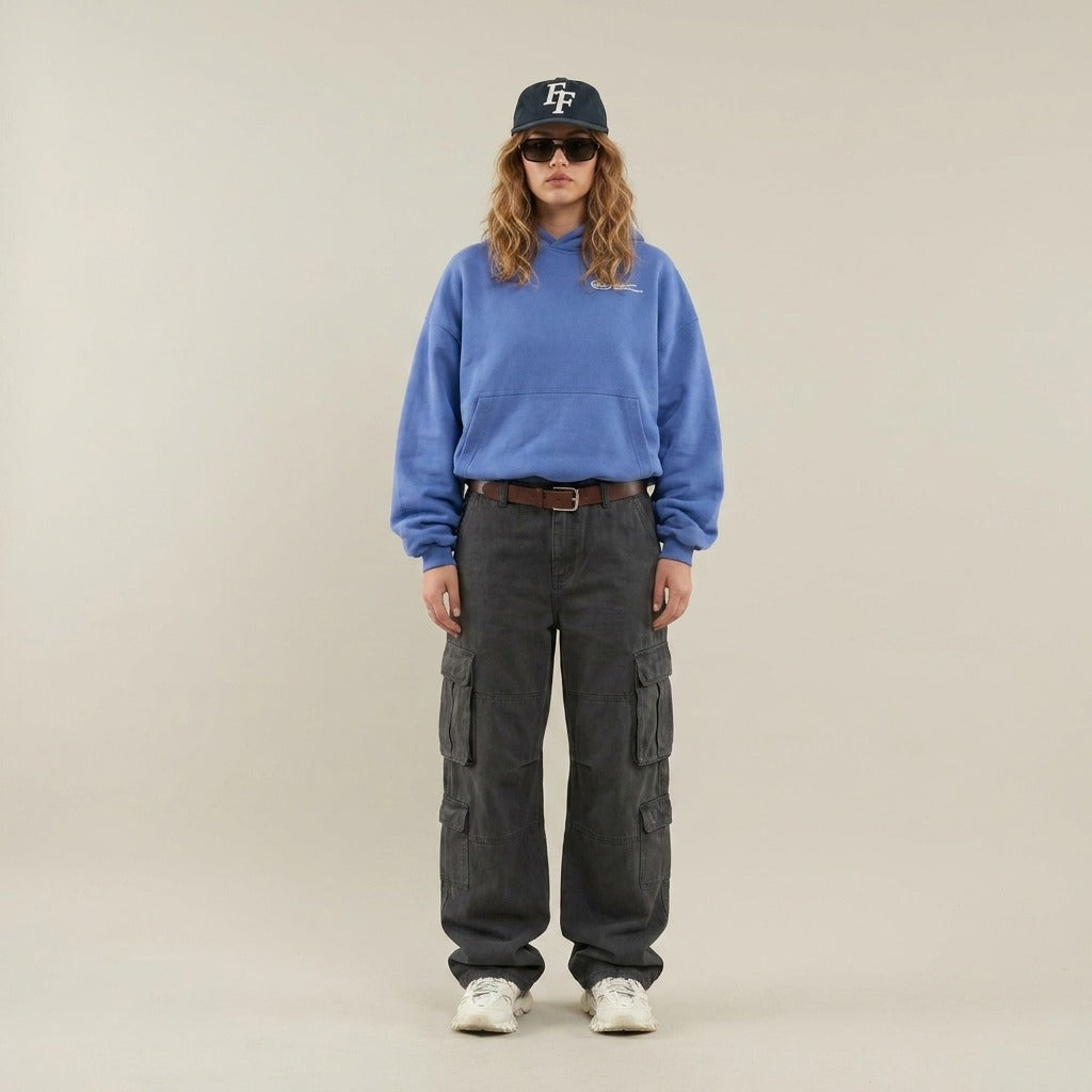 Vrouw in een blauwe oversized hoodie met een grijze cargobroek en een pet | Boutique Moda