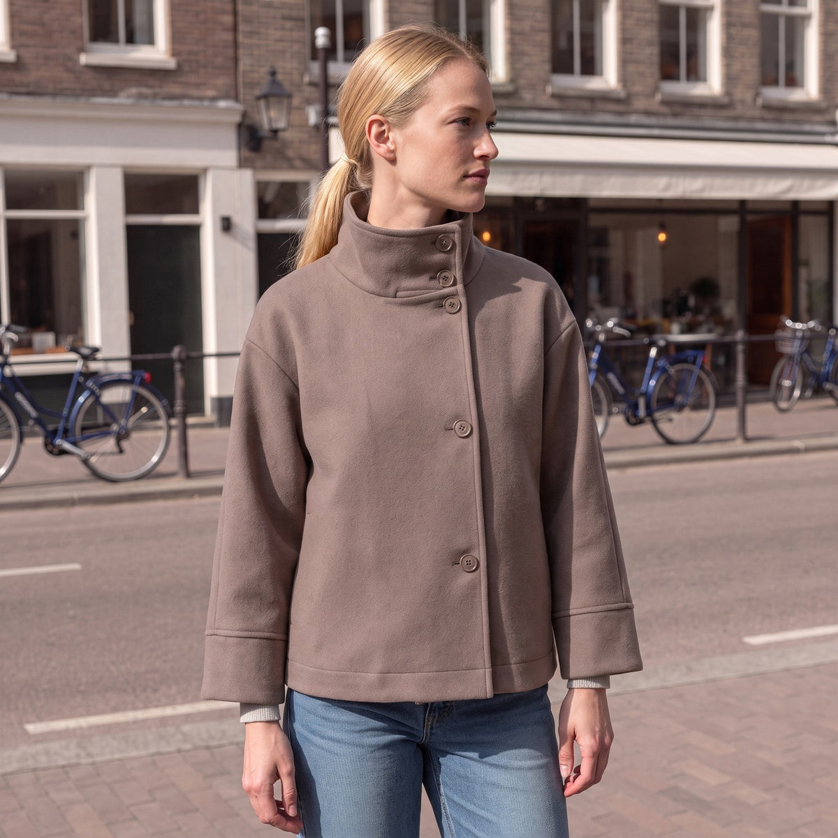 Vrouw in de taupe kort jasje met opstaande kraag in een Nederlandse straat | Boutique Moda