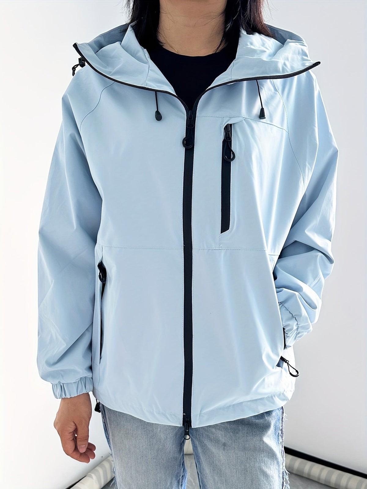 Lichtblauwe regenjas met capuchon, zwarte rits en borstzak | Boutique Moda