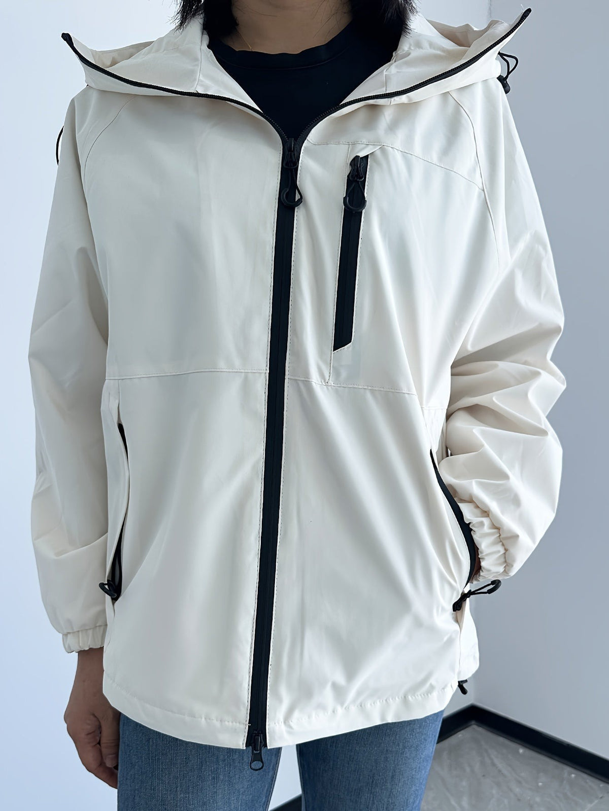 Ivoorkleurige regenjas met capuchon, zwarte rits en borstzak | Boutique Moda