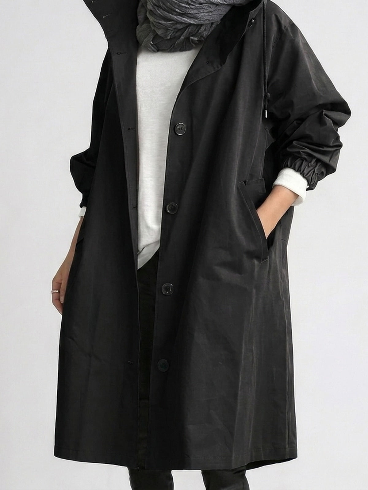 Trenchcoat met capuchon in zwart, open gedragen over een wit shirt | Boutique Moda