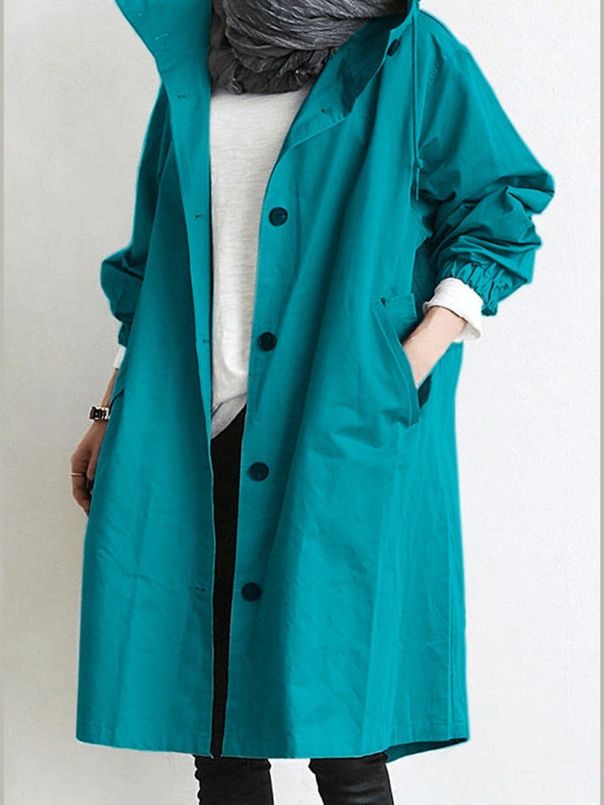 Trenchcoat met capuchon in turquoise, open gedragen over een wit shirt | Boutique Moda