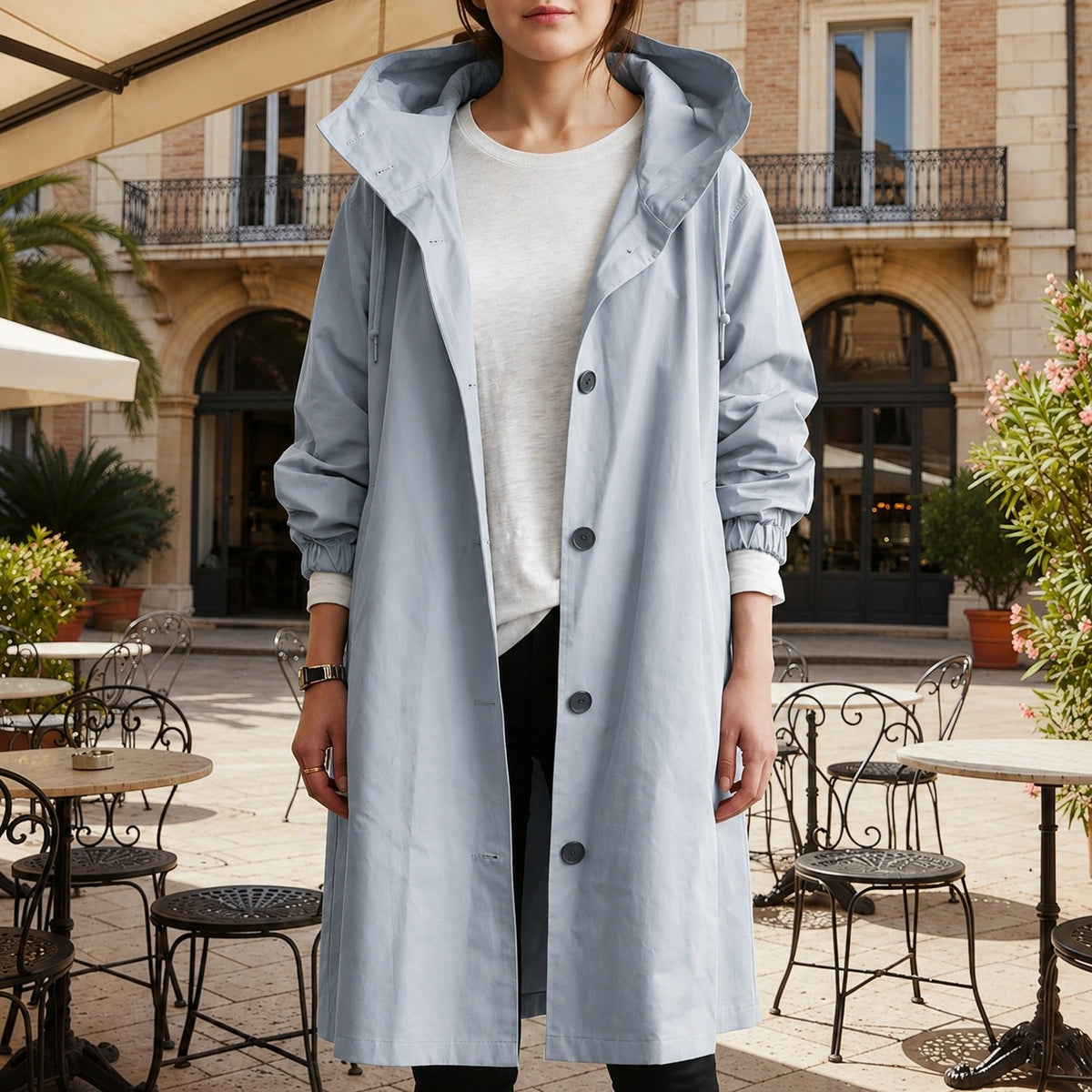 Lichtblauwe lange trenchcoat met capuchon en knoopsluiting, open gedragen over een wit T-shirt | Boutique Moda