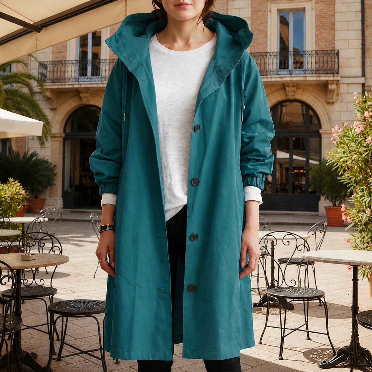 Petrolkleurige lange trenchcoat met capuchon en knoopsluiting, open gedragen over een wit T-shirt | Boutique Moda