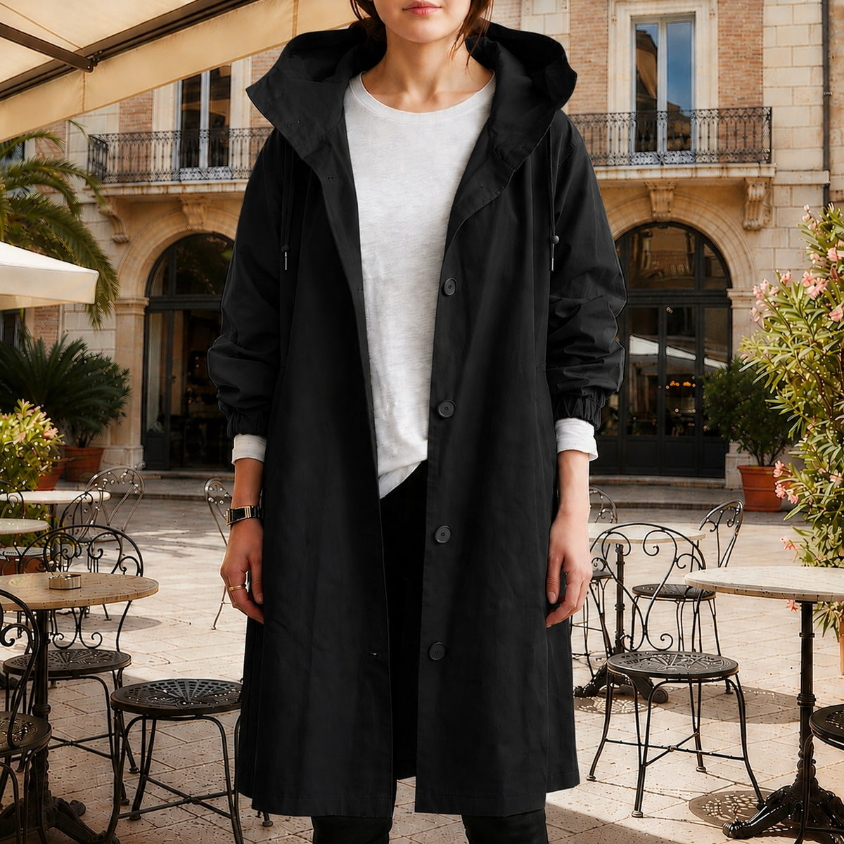 Zwarte lange trenchcoat met capuchon en knoopsluiting, open gedragen over een wit T-shirt | Boutique Moda