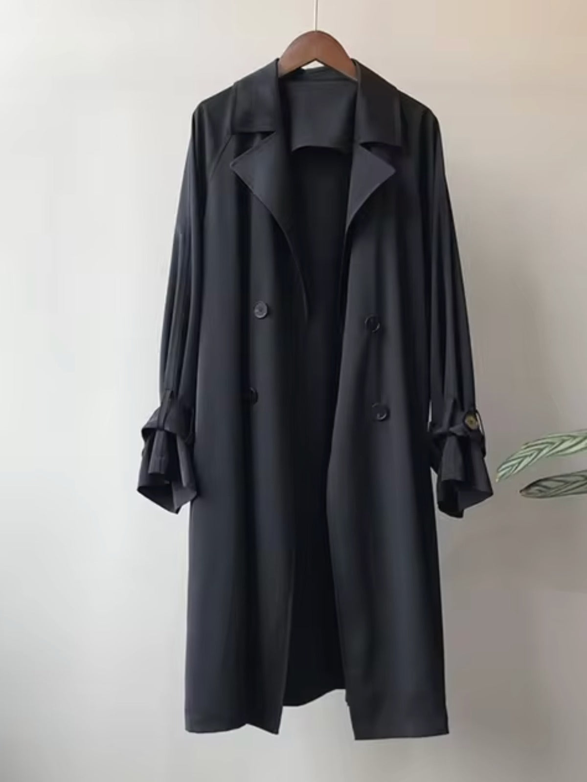 Lange trenchcoat met dubbele knopenrij in zwart aan een hanger | Boutique Moda