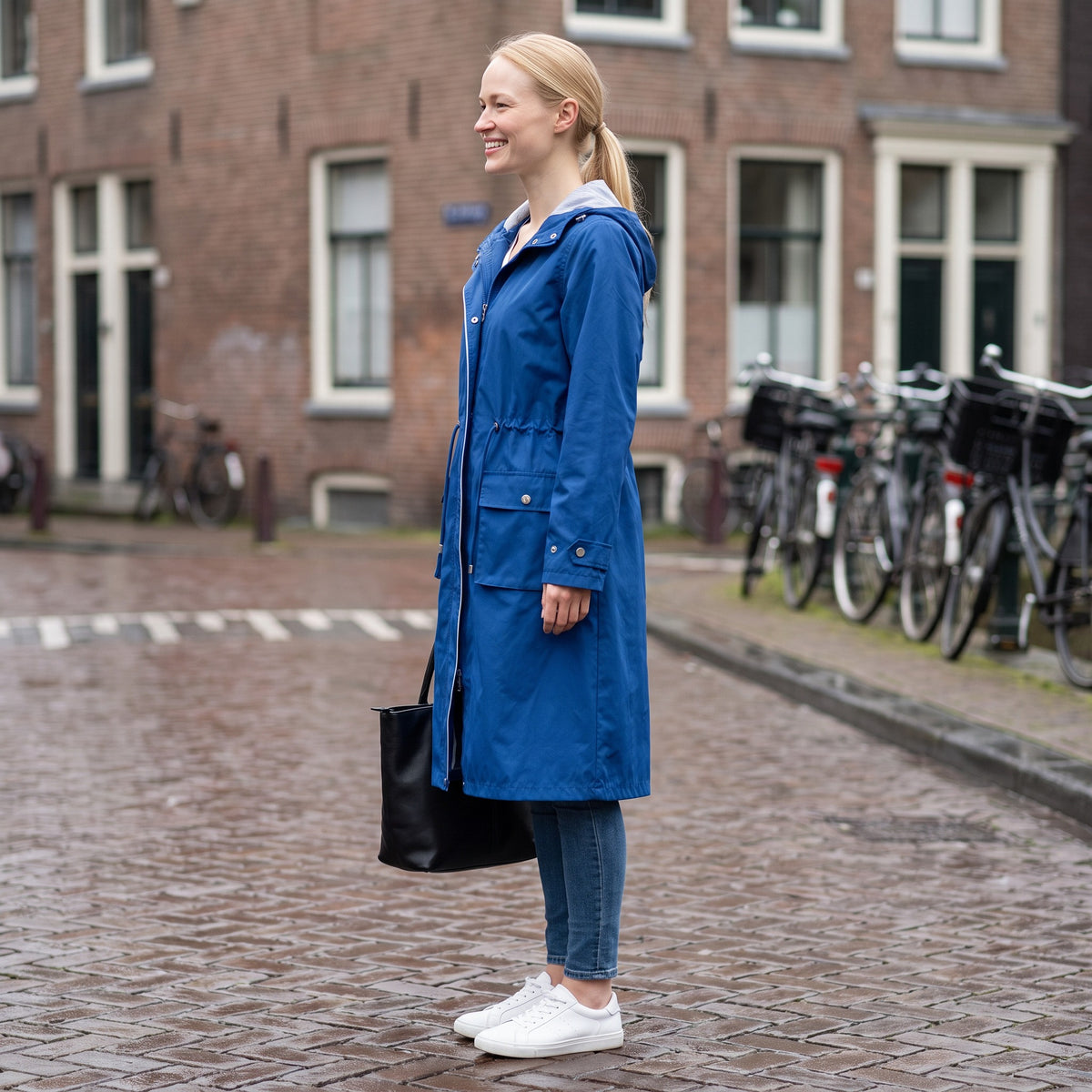 Zijkant van de blauwe lange regenjas met capuchon, gedragen op een natte straat | Boutique Moda