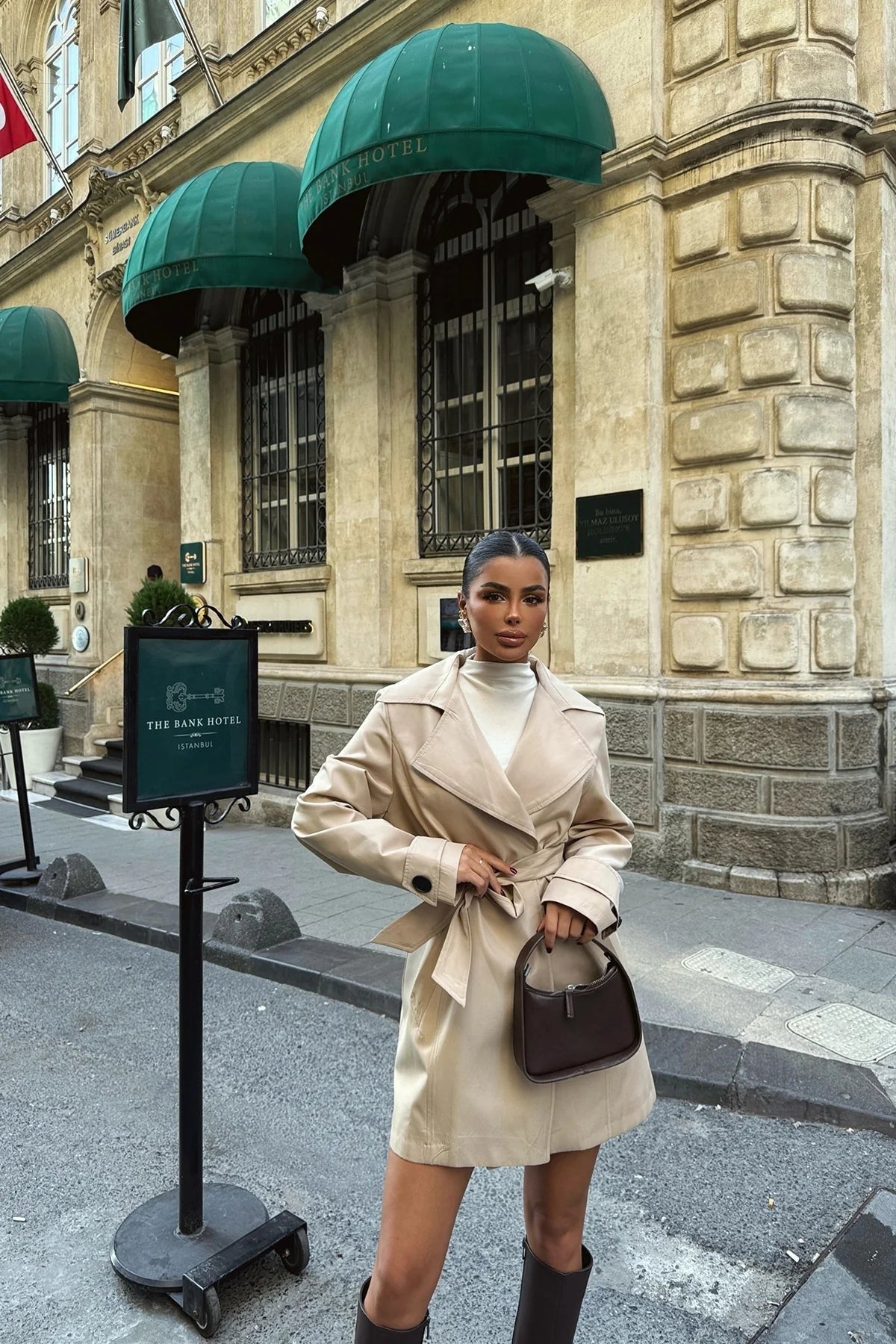 Beige korte trenchcoat met ceintuur in de taille, met een coltrui en een bruine tas | Boutique Moda