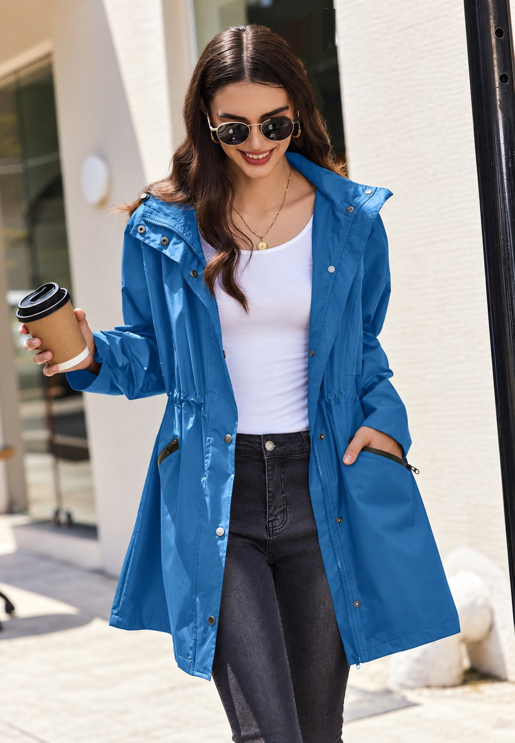 Vrouw in een blauwe waterdichte parka, open gedragen over een wit shirt, capuchon niet op | Boutique Moda