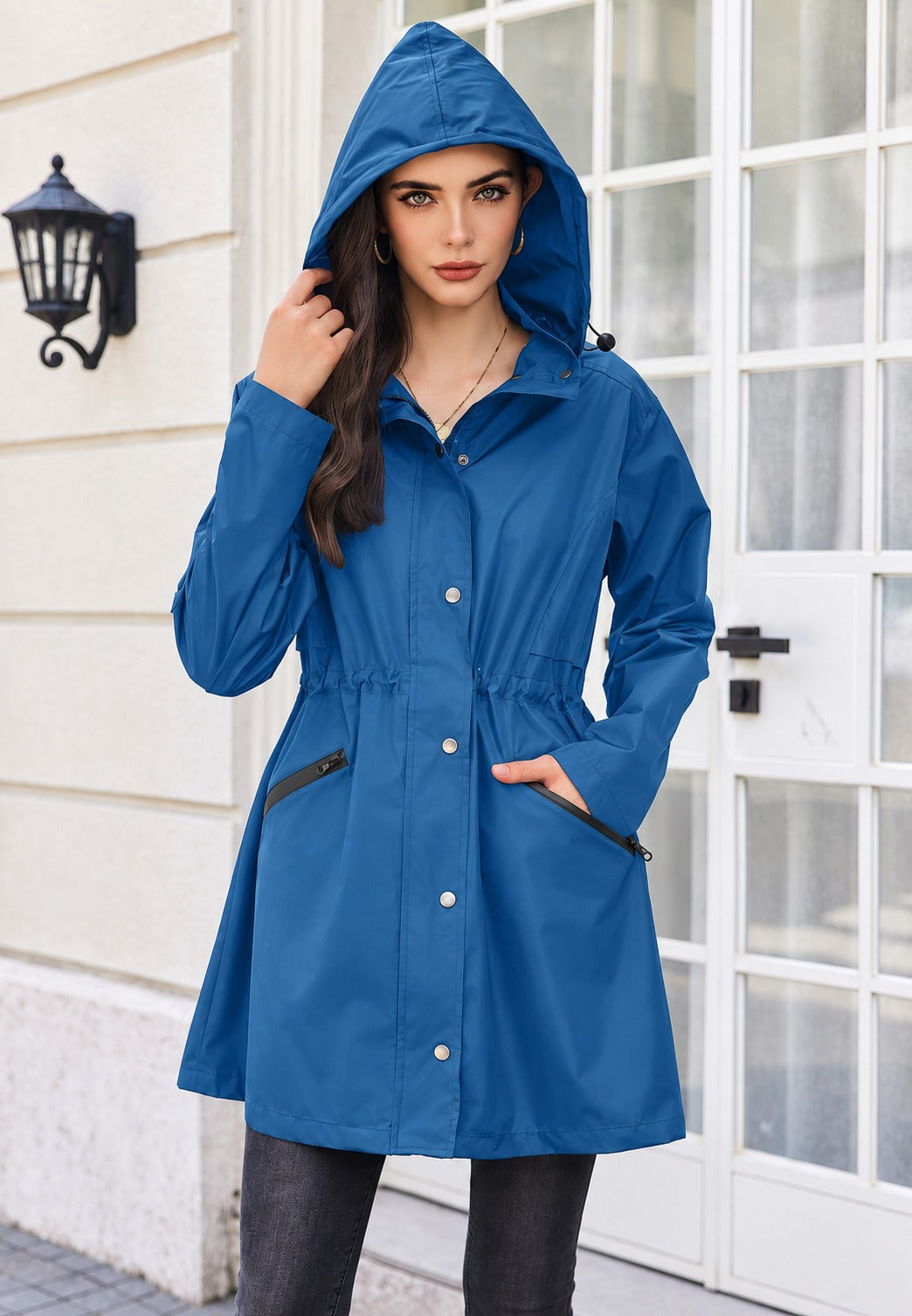 Blauwe parka dicht gedragen met de capuchon op, een hand in de zak met rits | Boutique Moda