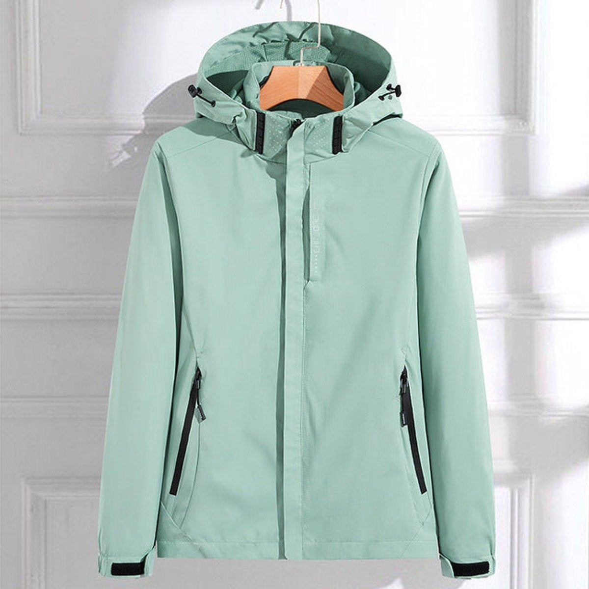 Mintgroen waterdicht windjack met capuchon en ritszakken met zwarte rand, aan een kledinghanger | Boutique Moda