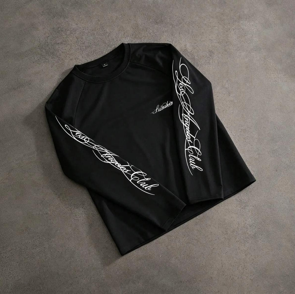 Zwarte longsleeve met sierlijke handschrift-print, plat gefotografeerd op grijze ondergrond | Boutique Moda