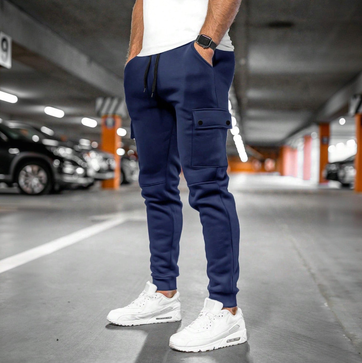 Donkerblauwe joggingbroek met cargozak, gedragen door man in parkeergarage | Boutique Moda