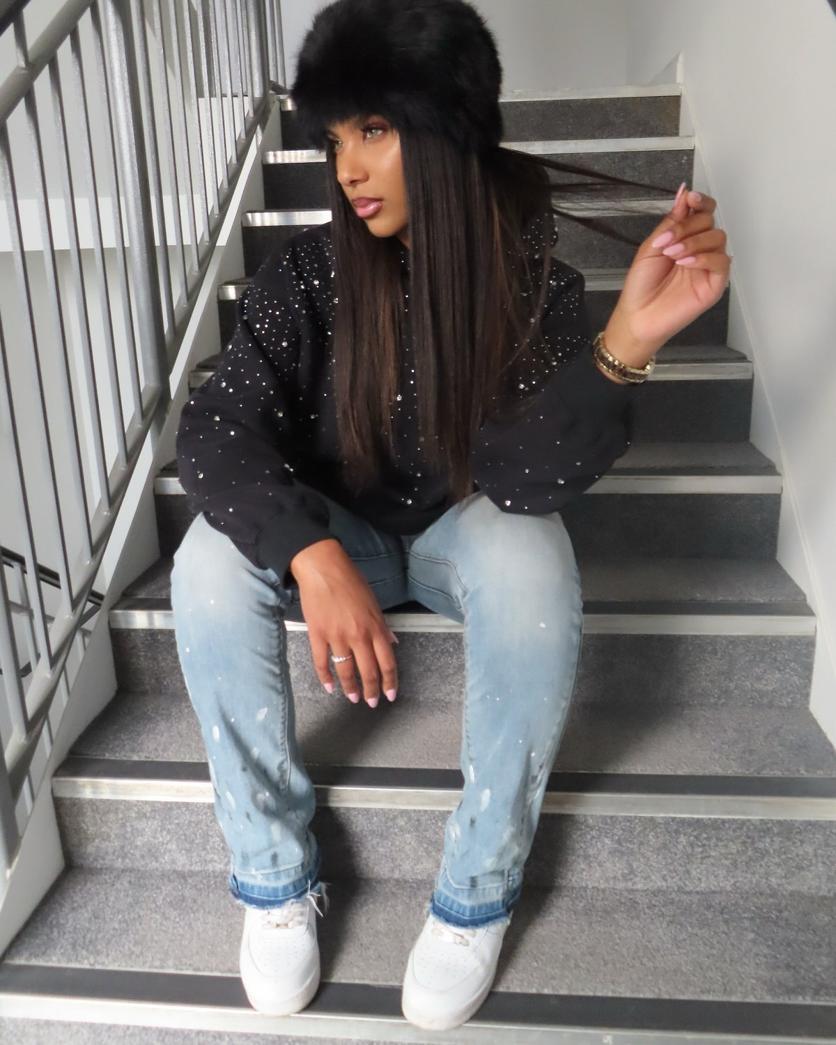 Vrouw in een zwarte hoodie met strass op een trap