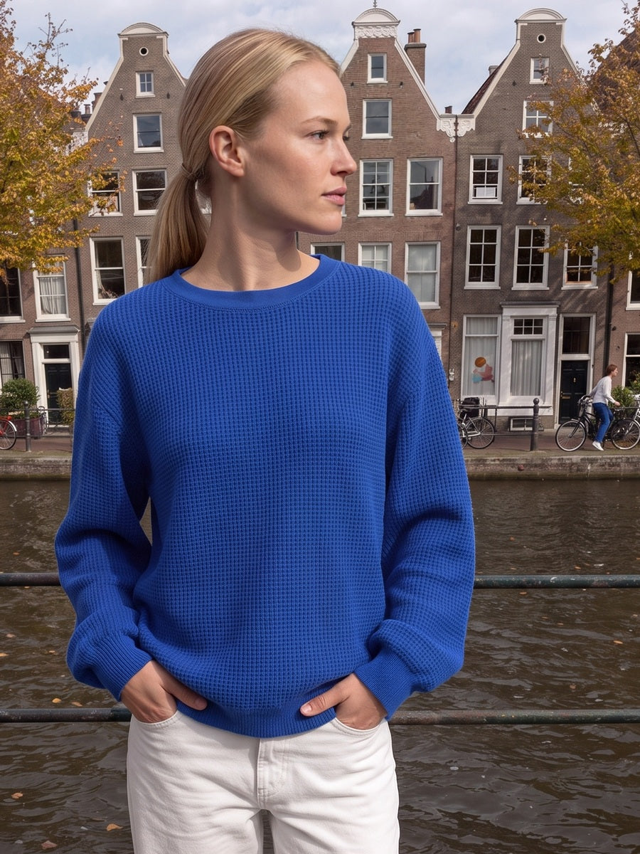 Vrouw in een kobaltblauwe oversized sweater met wafelstructuur aan een Amsterdamse gracht