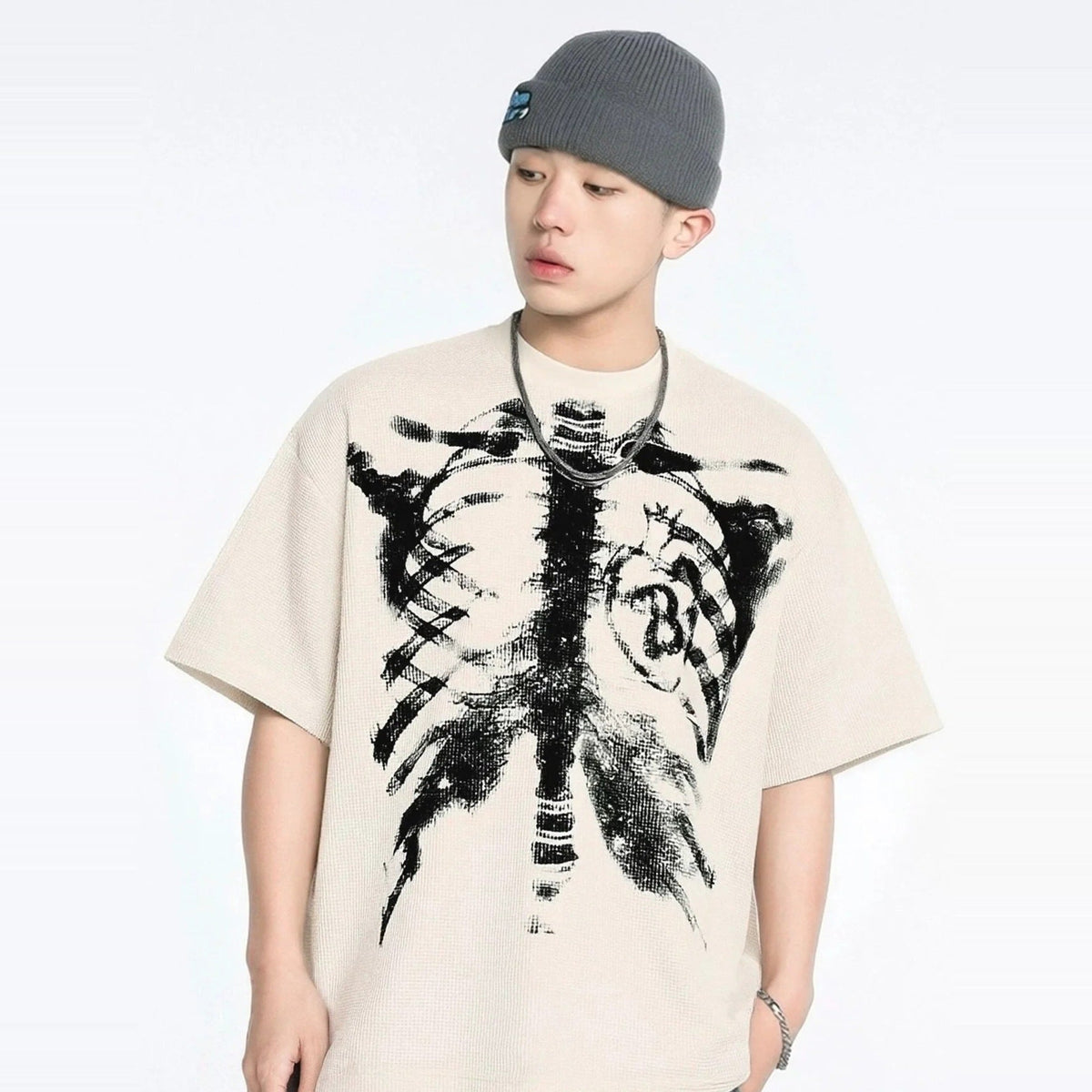 Beige oversized T-shirt met skeletprint, gedragen door jonge man met muts | Boutique Moda