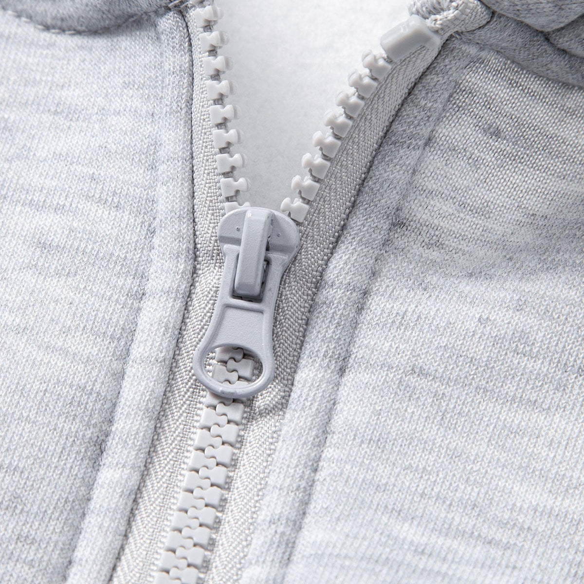 Close-up van grijze rits op lichtgrijs gemêleerd kledingstuk met capuchon | Boutique Moda