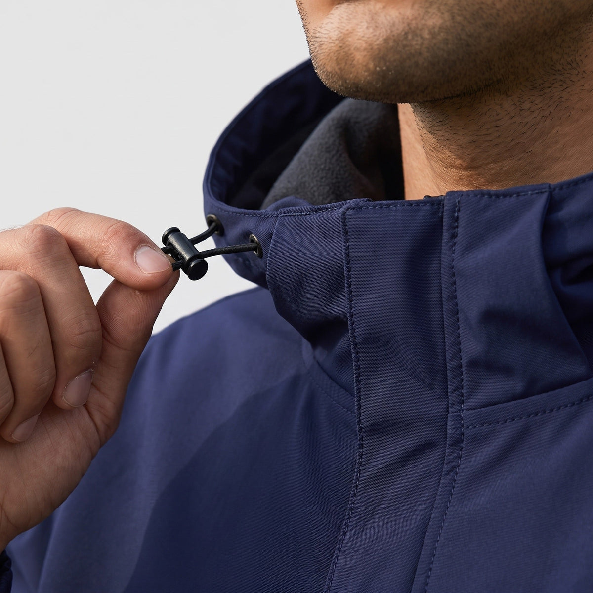 Man draagt donkerblauwe regenjas, close-up van capuchon koordstopper bij hals | Boutique Moda