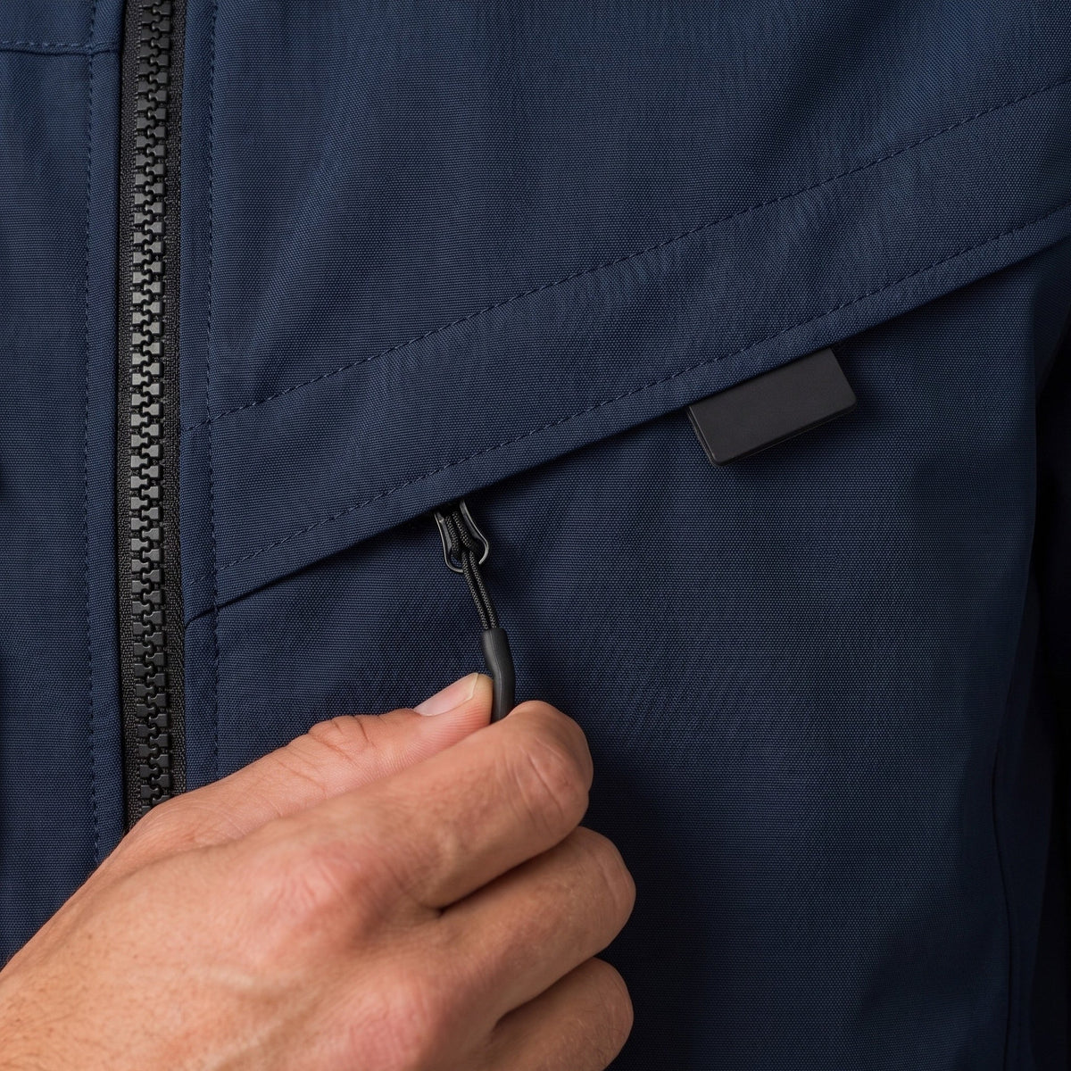 Close-up donkerblauwe jas met ritszak, hand opent trekkerlipje | Boutique Moda