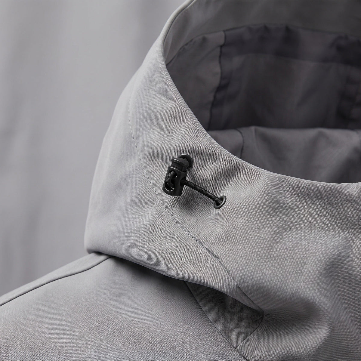 Close-up van grijze jas met kraag en zwarte metalen koordstopper detail | Boutique Moda