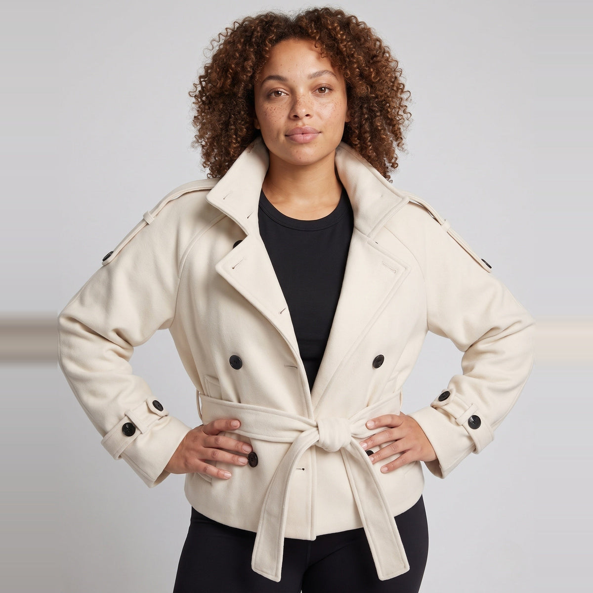 Vrouw draagt korte beige capejas met ceintuur en opstaande kraag | Boutique Moda