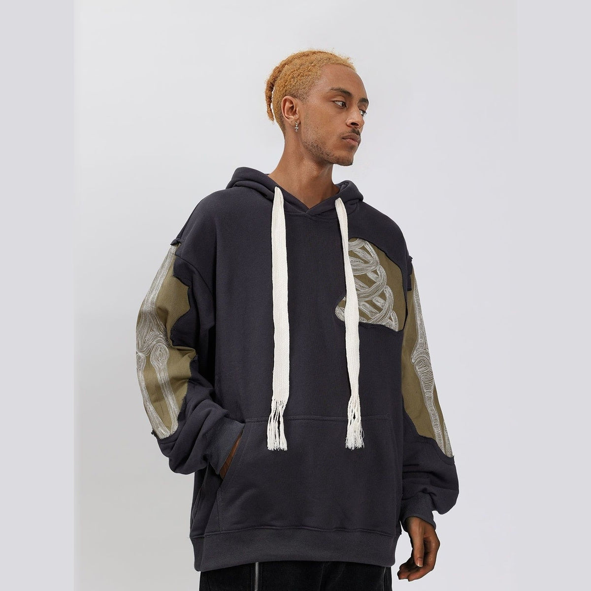 Donkergrijze oversized hoodie met camouflage patchwork, gedragen door man met trekkoorden | Boutique Moda