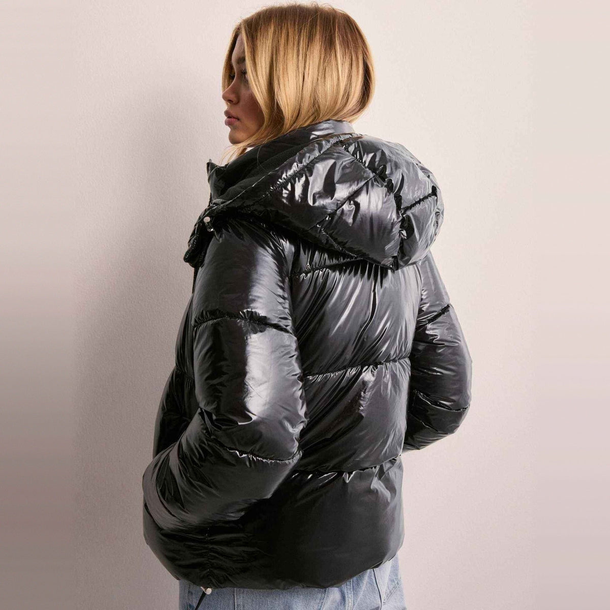 Zwarte glanzende gewatteerde jas met capuchon, gedragen door vrouw op rug | Boutique Moda