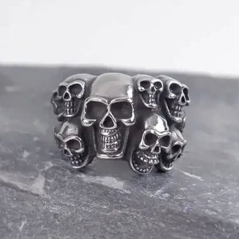 Zilverkleurige ring met meerdere schedels, plat neergelegd op stenen ondergrond | Boutique Moda