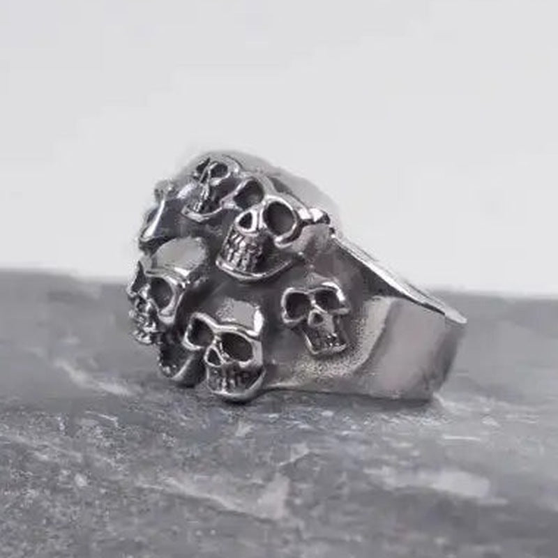 Zilverkleurige ring met meerdere schedels, liggend op donkere stenen ondergrond | Boutique Moda