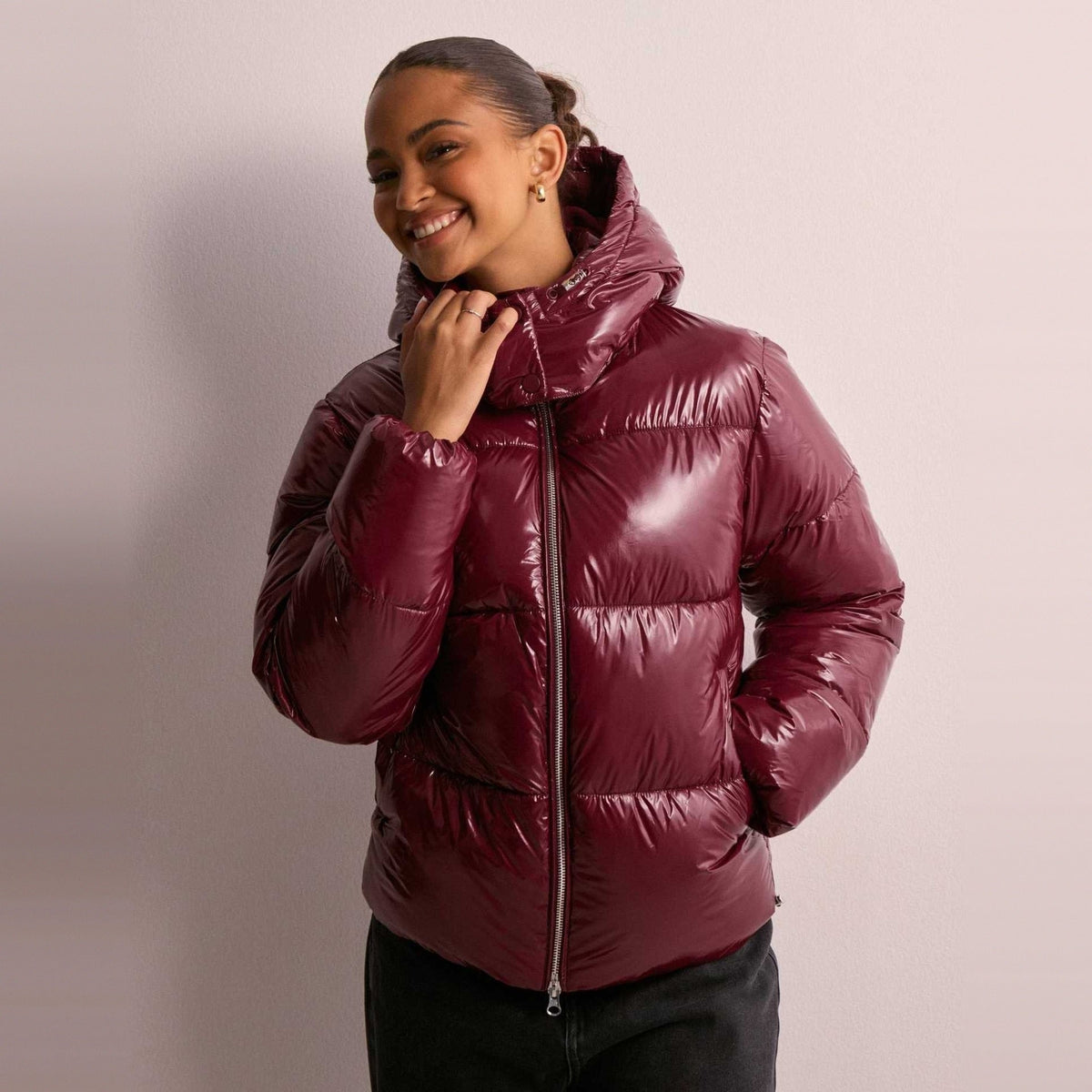 Glanzende bordeauxrode gewatteerde jas met capuchon, gedragen door glimlachende vrouw | Boutique Moda