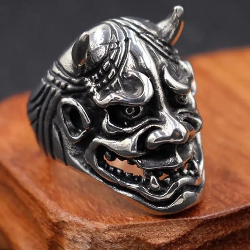 Zilverkleurige ring met gedetailleerd oni-demonenmasker en hoorns, op houten ondergrond | Boutique Moda