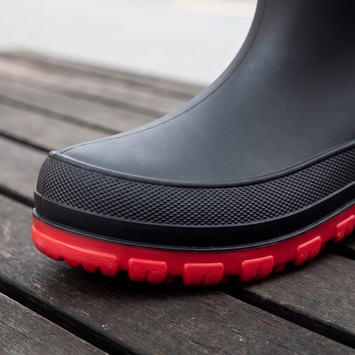 Zwarte regenlaars met rode geprofileerde zool, close-up op houten vlonder | Boutique Moda
