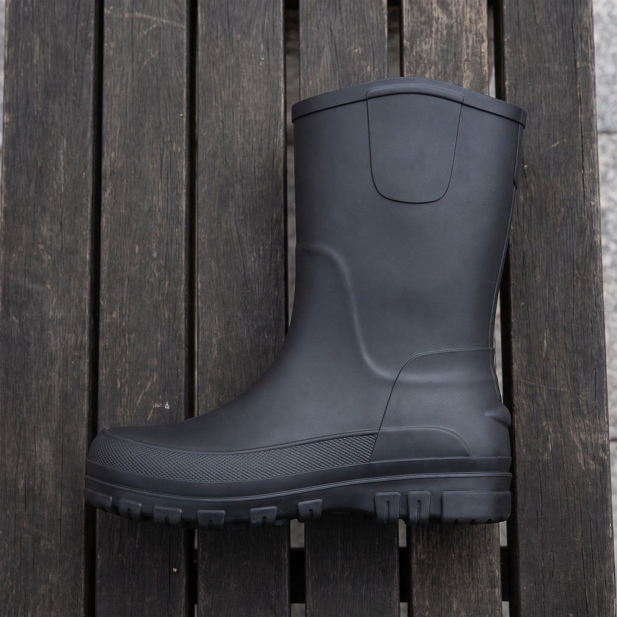 Zwarte halfhoge regenlaars, plat liggend op houten planken buiten | Boutique Moda