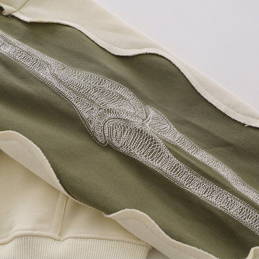 Close-up van beige hoodie met kaki paneel en geborduurd skeletpatroon | Boutique Moda