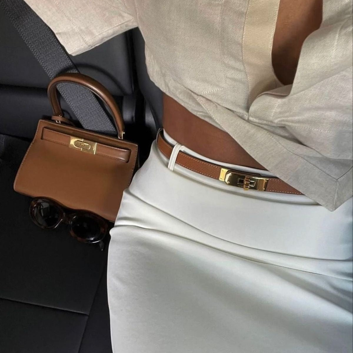 Bruine smalle riem van kunstleer met goudkleurige draaisluiting, gedragen op een witte rok | Boutique Moda